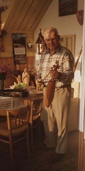 Mężczyzna stoi w pomieszczeniu przed stołem. W rękach trzyma drewniany instrument muzyczny - złóbcoki.