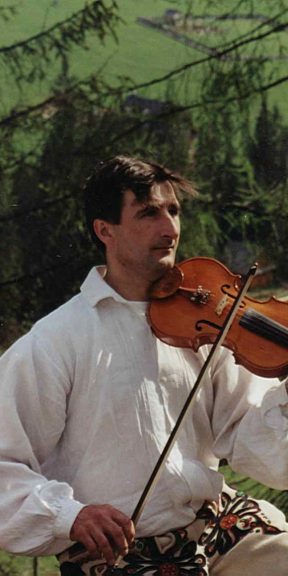 Mężczyzna w białej koszuli gra na skrzypcach.
