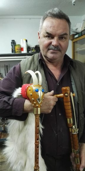 Mężczyzna z krótkimi włosami trzyma w rękach instrument muzyczny z główką z rogami.